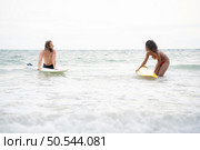 Young men teaching surfing with a surfboard with young women in red swimsuits. Стоковое фото, агентство Ingram Publishing / Фотобанк Лори