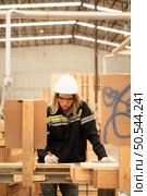 Female carpenter working in a woodworking factory, She is wearing a safety helmet and glasses. Checking the neatness of the planks against the design documents. Стоковое фото, агентство Ingram Publishing / Фотобанк Лори
