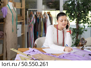Busy young tailoress working with document while talking on phone. Стоковое фото, фотограф Яков Филимонов / Фотобанк Лори