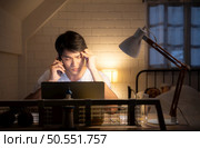 Young man using laptop and talking on the phone while sitting at home with headaches that recur when stressed. Стоковое фото, агентство Ingram Publishing / Фотобанк Лори