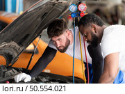 Car mechanic working in an auto repair shop, inspecting the operation of the car’s air conditioner and refrigerant. Стоковое фото, агентство Ingram Publishing / Фотобанк Лори
