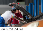 Car mechanic working in an auto repair shop explain to customer after inspecting the operation of the car’s air conditioner and refrigerant. Стоковое фото, агентство Ingram Publishing / Фотобанк Лори