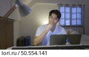 Young Asian man working overtime at home take medicine and drink water to relieve stress and headaches. Стоковое фото, агентство Ingram Publishing / Фотобанк Лори