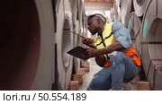 A young men working in a warehouse storing rolls of metal sheets. Inspecting the metal sheet rolls stored in the warehouse to be imported onto the metal sheet production line. Стоковое фото, агентство Ingram Publishing / Фотобанк Лори