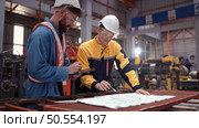 Team of engineers and architects working with blueprint at factory site. It is a massive new facility for making metal sheets as well as a transportation and distribution warehouse. Стоковое фото, агентство Ingram Publishing / Фотобанк Лори
