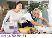 Focused young repairman repairing sewing-machine and Asian tailoress talking. Стоковое фото, фотограф Яков Филимонов / Фотобанк Лори