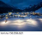 Aerial view of beautiful alpine village at cold winter night. Kranjska Gora, Slovenia. Top drone view of buildings in snow, street lights, road, snowy alpine mountains, sky at dusk. Triglav park. Стоковое фото, агентство Ingram Publishing / Фотобанк Лори