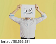 Young businessman holding white card with a sad face on it isolated on Yellow background. Стоковое фото, агентство Ingram Publishing / Фотобанк Лори