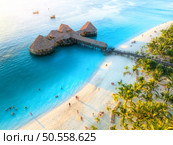 Aerial view of beautiful bungalow in Indian ocean at sunset in summer. Restaurant on the sea. Top view of wooden hotel, palm trees, azure water, white sandy beach. Luxury resort in Kendwa, Zanzibar. Стоковое фото, агентство Ingram Publishing / Фотобанк Лори