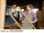 Portrait of carpenter female worker standing in front of colleague in workshop, Eyesight is utilized to ensure accuracy. Стоковое фото, агентство Ingram Publishing / Фотобанк Лори