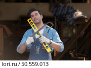 Portrait of a carpenter holding a spirit level and handsaw in his workshop. Стоковое фото, агентство Ingram Publishing / Фотобанк Лори