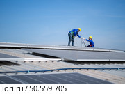 A young technician intern working on solar panels is fear of heights with senior engineers who are always helping out. Стоковое фото, агентство Ingram Publishing / Фотобанк Лори