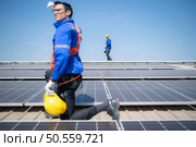 Technician repairing solar panels take off his hat and rest in the scorching sun on a factory roof covered with solar panels to receive solar energy. Стоковое фото, агентство Ingram Publishing / Фотобанк Лори
