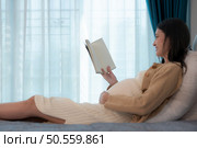 Pregnant woman reading a stories to her unborn child in the living room at home. Стоковое фото, агентство Ingram Publishing / Фотобанк Лори