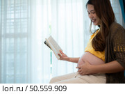 Pregnant woman reading a stories to her unborn child in the living room at home. Стоковое фото, агентство Ingram Publishing / Фотобанк Лори