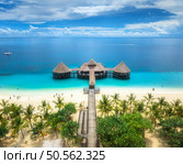 Aerial view of bungalow, white sandy beach, ocean on summer sunny day. Restaurant on the sea. Top drone view of wooden hotel, azure water, palms, sky with slouds. Luxury resort in Kendwa, Zanzibar. Стоковое фото, агентство Ingram Publishing / Фотобанк Лори