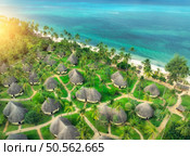 Aerial view of green palms, bungalows, grass, sandy beach, blue ocean at sunset in summer. Top view of wooden houses, sea with azure water, palms. Luxury resort in Zanzibar. Tropical background. Стоковое фото, агентство Ingram Publishing / Фотобанк Лори