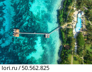 Aerial view of bungalow, jetty, white sandy beach, ocean on summer sunny day. Restaurant on the sea. Top drone view of wooden hotel, azure water, pool, green palms. Luxury resort in Zanzibar. Tropical. Стоковое фото, агентство Ingram Publishing / Фотобанк Лори