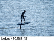 Surfer glides above calm water on electric hydrofoil board, demonstrating advanced water sports technology in a serene marine setting. Стоковое фото, агентство Ingram Publishing / Фотобанк Лори