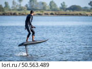 A man glides effortlessly on an electric hydrofoil surfboard, maintaining balance while enjoying a smooth ride on calm waters. Стоковое фото, агентство Ingram Publishing / Фотобанк Лори