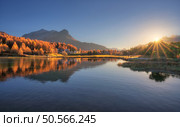 The tranquil Silvaplana lake glows in the golden rays at sunrise. Reflecting the vibrant colors of autumn trees and the majestic swiss alps. Landscape with orange trees, mountains. Fall in Switzerland. Стоковое фото, агентство Ingram Publishing / Фотобанк Лори