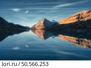 Sunset casts a serene glow on mountain peaks mirrored in a tranquil alpine lake in autumn. Lake Bianco, Switzerland in fall. Landscape with mountains, reflection in water, blue sky. Picturesque scene. Стоковое фото, агентство Ingram Publishing / Фотобанк Лори