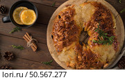 Festive wreath bread with nuts and honey glaze on a wooden board, accompanied by a cup of hot beverage with orange slices, cinnamon sticks, and pinecones. Стоковое фото, агентство Ingram Publishing / Фотобанк Лори