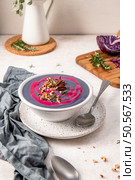 Purple soup garnished with pecans and rosemary in a white bowl on a speckled plate, accompanied by a spoon and a gray napkin, with a cutting board and herbs in the background. Стоковое фото, агентство Ingram Publishing / Фотобанк Лори