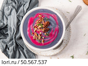 Purple soup with pink swirl, topped with pecans and rosemary, served in a speckled bowl with a spoon on a white plate, next to a gray cloth. Стоковое фото, агентство Ingram Publishing / Фотобанк Лори