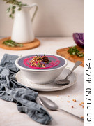 Purple soup garnished with nuts and herbs in a white bowl on a speckled plate, with a spoon and gray cloth napkin beside it, set on a light surface. Стоковое фото, агентство Ingram Publishing / Фотобанк Лори