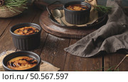 Three ramekins of creamy custard with a caramelized sugar crust, on a rustic wooden table with pine branches. Стоковое фото, агентство Ingram Publishing / Фотобанк Лори