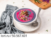 Purple and pink soup garnished with pecans and rosemary, served in a white bowl on a speckled plate with a spoon, and a gray cloth napkin beside it. Стоковое фото, агентство Ingram Publishing / Фотобанк Лори