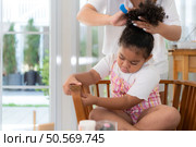 The mother helps her daughter get ready and ties her hair to make it seem neat. Стоковое фото, агентство Ingram Publishing / Фотобанк Лори
