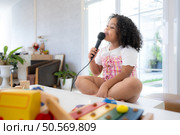 A tiny girl sits on a toy table, clutching a microphone, and sings cheerfully in the living room. Стоковое фото, агентство Ingram Publishing / Фотобанк Лори