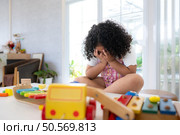 A little girl sits sadly, covering her face with her hands, in the living room. Стоковое фото, агентство Ingram Publishing / Фотобанк Лори