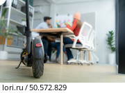 Selective focus of electric scooter in modern office with group meeting blurred background. Стоковое фото, агентство Ingram Publishing / Фотобанк Лори