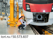 Portrait of a young female technician using a blueprint working and standing in a skytrain repair station. Стоковое фото, агентство Ingram Publishing / Фотобанк Лори
