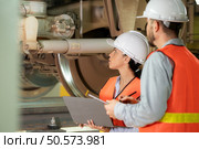 Male and female engineers work together in an electric repair station. Inspecting the undercarriage of electric train that are being repaired at the garage. Стоковое фото, агентство Ingram Publishing / Фотобанк Лори