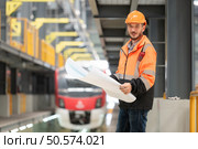Portrait of a young male technician using a blueprint working and standing in a skytrain repair station. Стоковое фото, агентство Ingram Publishing / Фотобанк Лори
