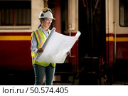 Portrait of railway technician worker in safety vest and helmet working with blueprint at train repair station. Стоковое фото, агентство Ingram Publishing / Фотобанк Лори