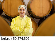 Smiling female winemaker in yellow uniform standing in cellar of winery. Стоковое фото, агентство Ingram Publishing / Фотобанк Лори