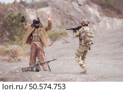 A Taliban soldier stands with a machine gun, Raise hands in surrender to the allied soldiers, In the desert mountain terrain battlefield. Стоковое фото, агентство Ingram Publishing / Фотобанк Лори
