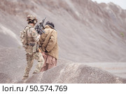 A Taliban soldier stands with a machine gun, Raise hands in surrender to the allied soldiers, In the desert mountain terrain battlefield. Стоковое фото, агентство Ingram Publishing / Фотобанк Лори