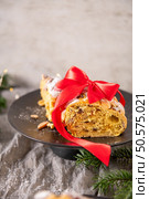 A festive slice of Bolo Rainha, adorned with a vibrant red ribbon, sits on a dark plate. The traditional Portuguese Christmas cake, rich with nuts and fruit, is ready for holiday celebrations. Стоковое фото, агентство Ingram Publishing / Фотобанк Лори