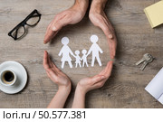 Close up of female and male hands protecting a paper chain family. Top view of two hands form a circle around white paper chain family on wooden table. Family care, insurance and helping hand concept. Стоковое фото, агентство Ingram Publishing / Фотобанк Лори