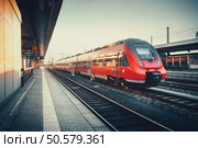 Beautiful railway station with modern red commuter train at colorful sunset in Nuremberg, Germany. Railroad with vintage toning. Стоковое фото, агентство Ingram Publishing / Фотобанк Лори