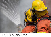 two firemen in helmet and oxygen mask spraying water to fire surround with smoke and dust. Стоковое фото, агентство Ingram Publishing / Фотобанк Лори