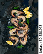 Fresh uncooked shrimps with lemon, herbs and spices on chipped ice over dark slate stone backdrop, top view. Fresh uncooked shrimps with lemon, herbs and spices on chipped ice over dark slate stone backdrop. Стоковое фото, агентство Ingram Publishing / Фотобанк Лори