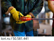 A very talented glassblower is forming and shaping glass in a studio for glass making. He is creating a fluted bowl from this piece of molten glass. Стоковое фото, агентство Ingram Publishing / Фотобанк Лори