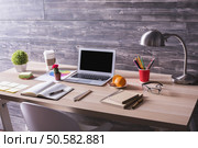 Side view of creative designer workplace with blank laptop, stationery items, lamp, orange and chocolate on plate and other items on wooden background. Mock up. Стоковое фото, агентство Ingram Publishing / Фотобанк Лори